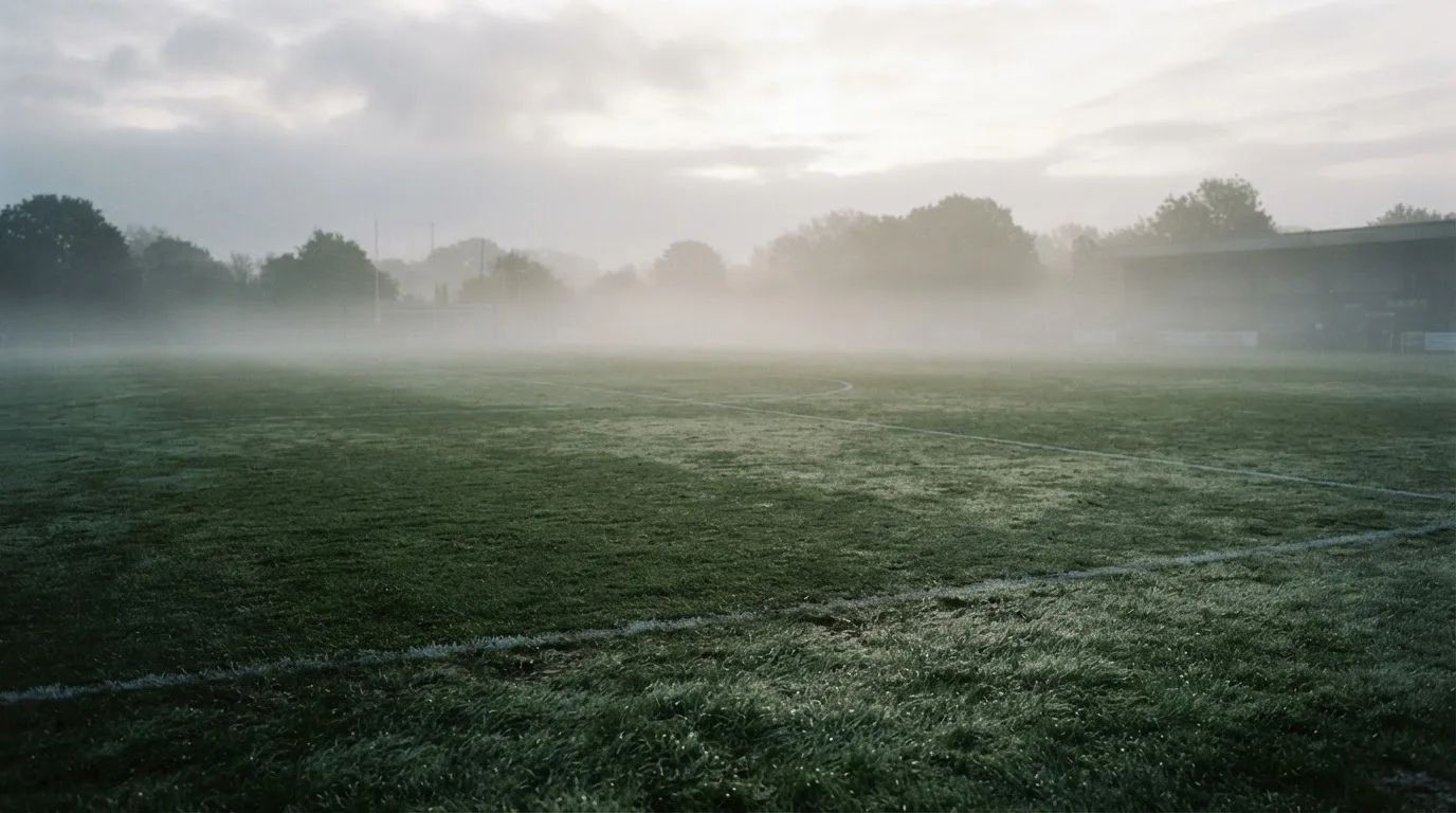Ein leeres Fußballfeld im Morgennebel, die Mittellinie verliert sich im Dunst, kein Mensch ist zu sehen.