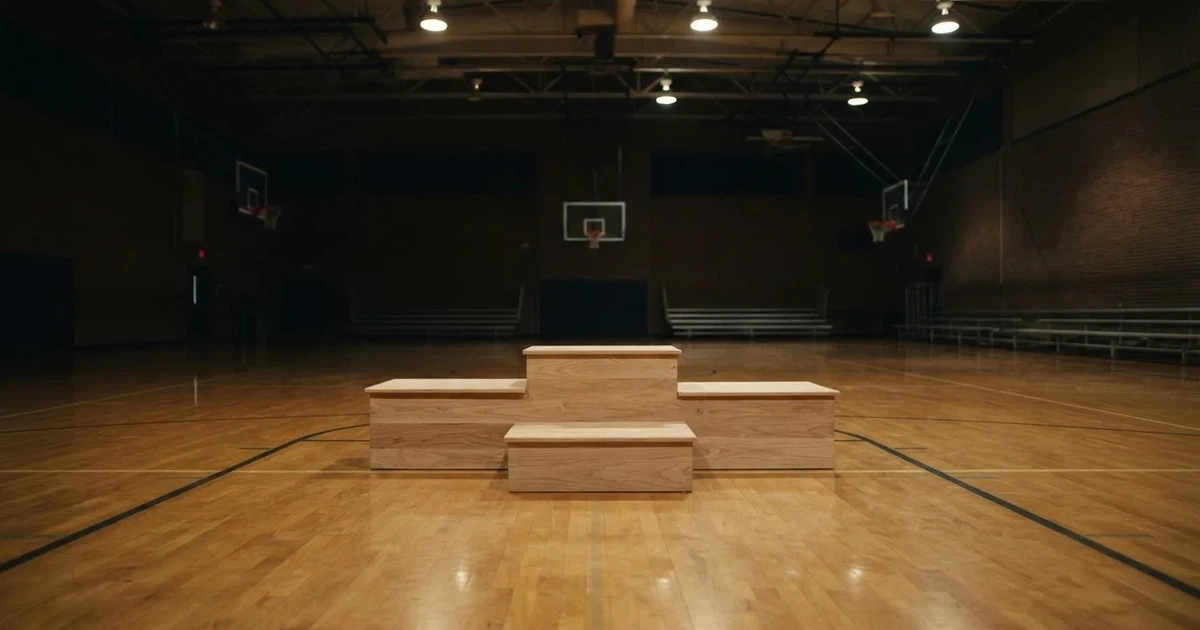 Ein Podium aus hellem Holz steht in einer leeren Sporthalle unter Hallenlicht, ohne Beschriftung oder Zahlen, niemand ist zu sehen.